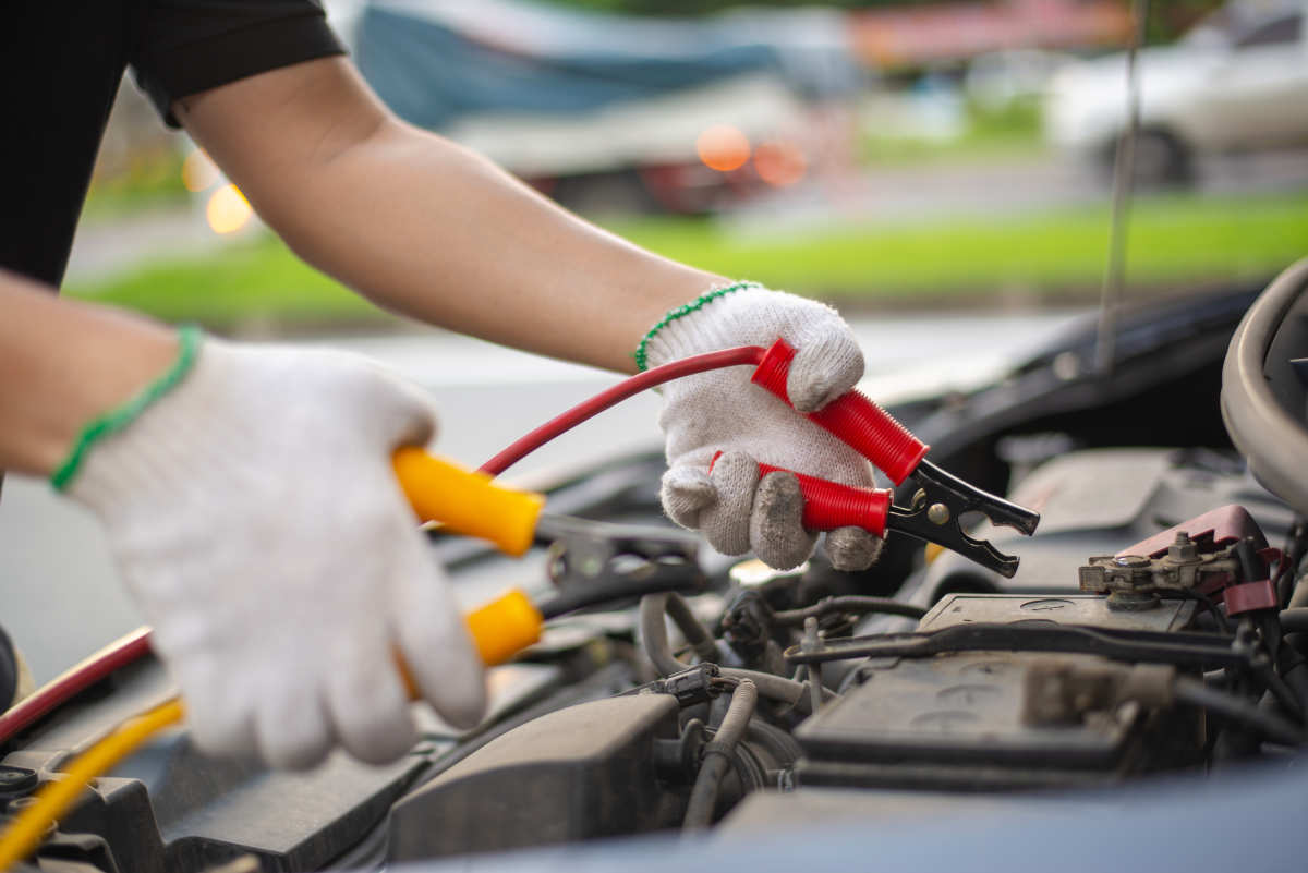 Young man charging battery car with electricity trough jumper cables on the country road, insurance and service concept. jump cables connecting to car battery to jumpstart car